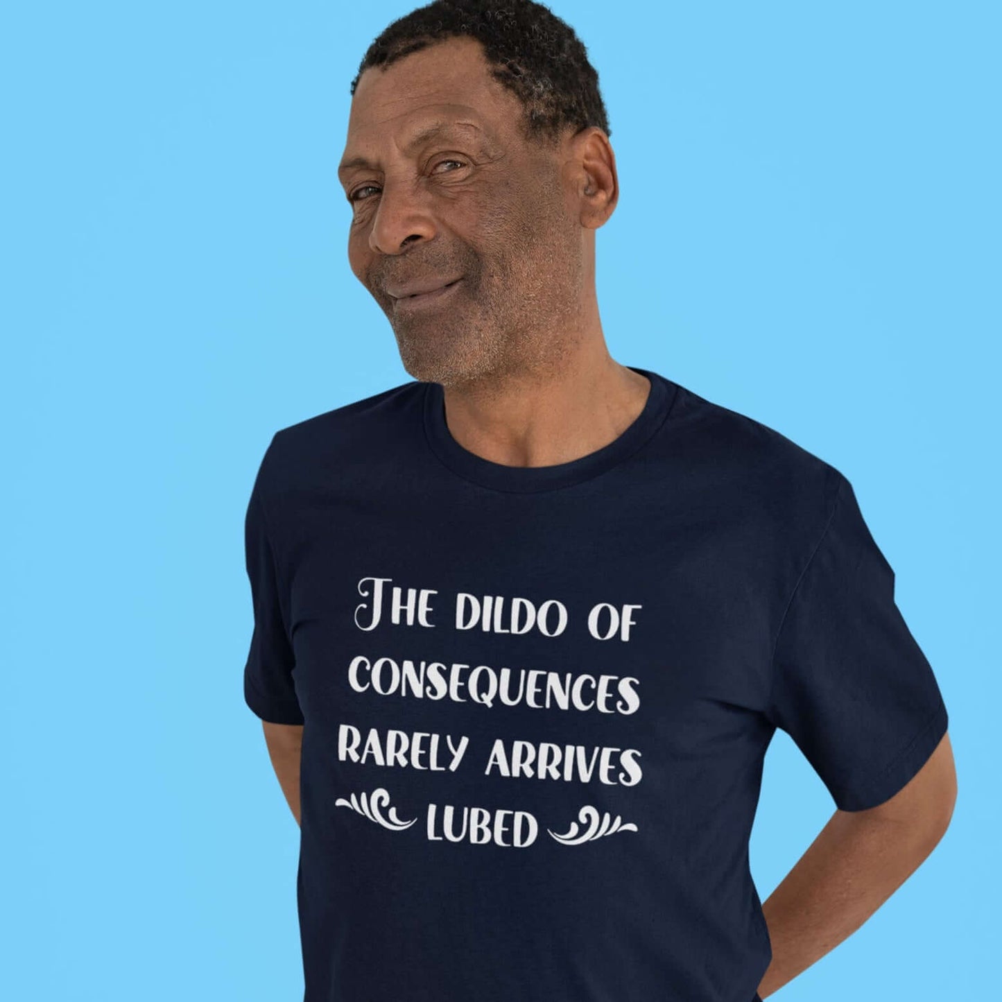 Smiling man wearing a navy blue t-shirt with the phrase The dildo of consequences rarely arrives lubed printed on the front.