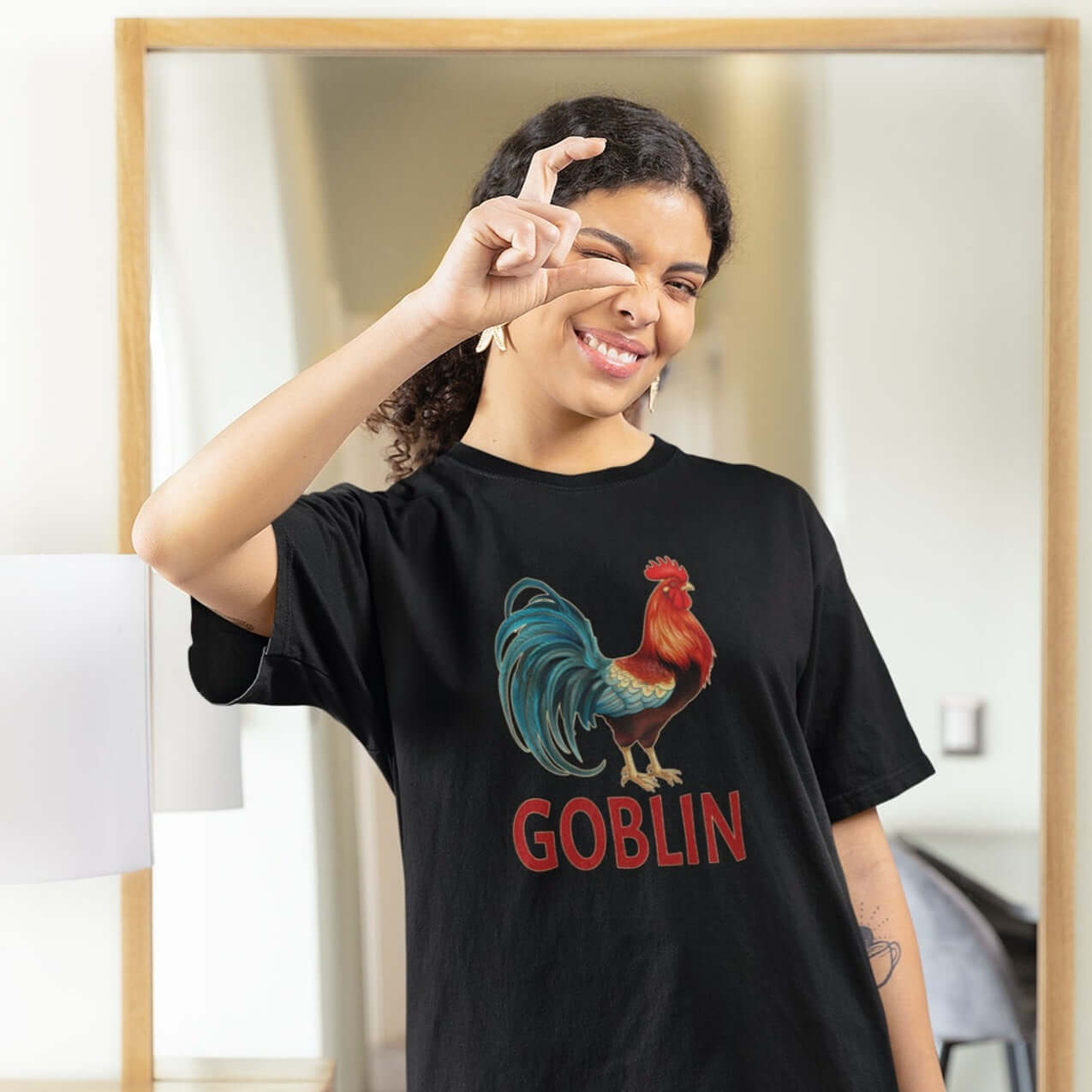 Woman wearing a black t-shirt with an image of a rooster and the word Goblin printed under the rooster. The graphics are printed on the front of the shirt.