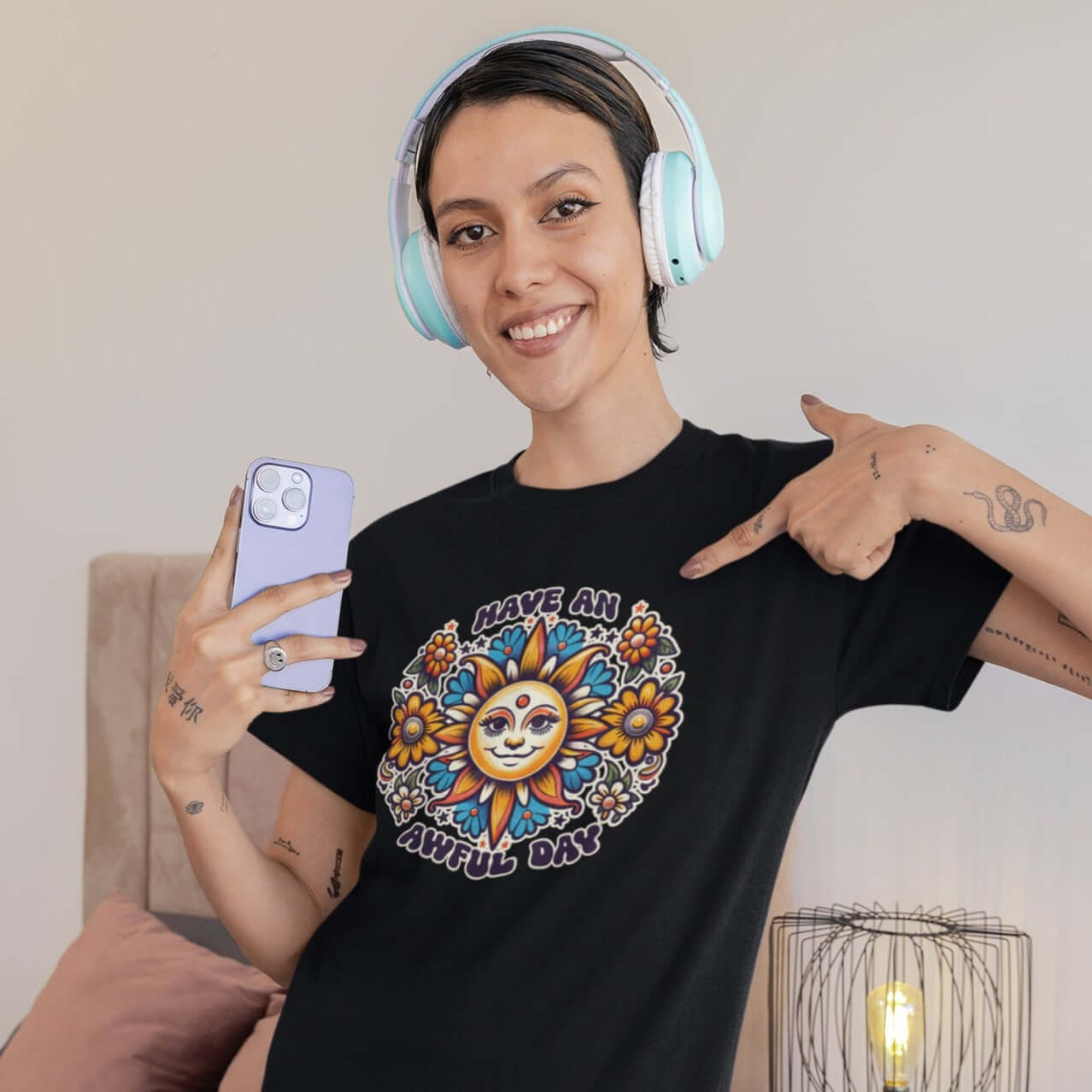 Woman wearing headphones and pointing at her shirt. She is wearing a black t-shirt with a sun graphic and the phrase Have an awful day printed on the front.