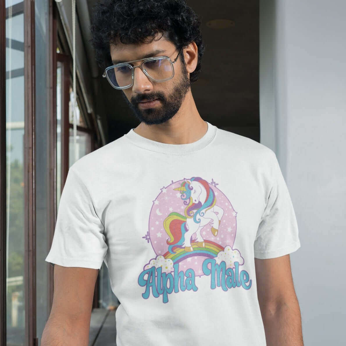 Bearded man wearing white t-shirt with funny pastel rainbow unicorn graphics and the words Alpha Male printed on the front.
