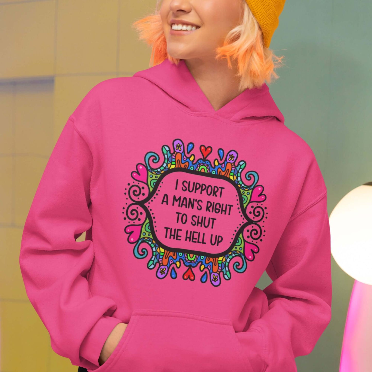 Woman wearing a heliconia pink color hoodie sweatshirt with a colorful doodle graphic and the words I support a man's right to shut the hell up printed on the front.