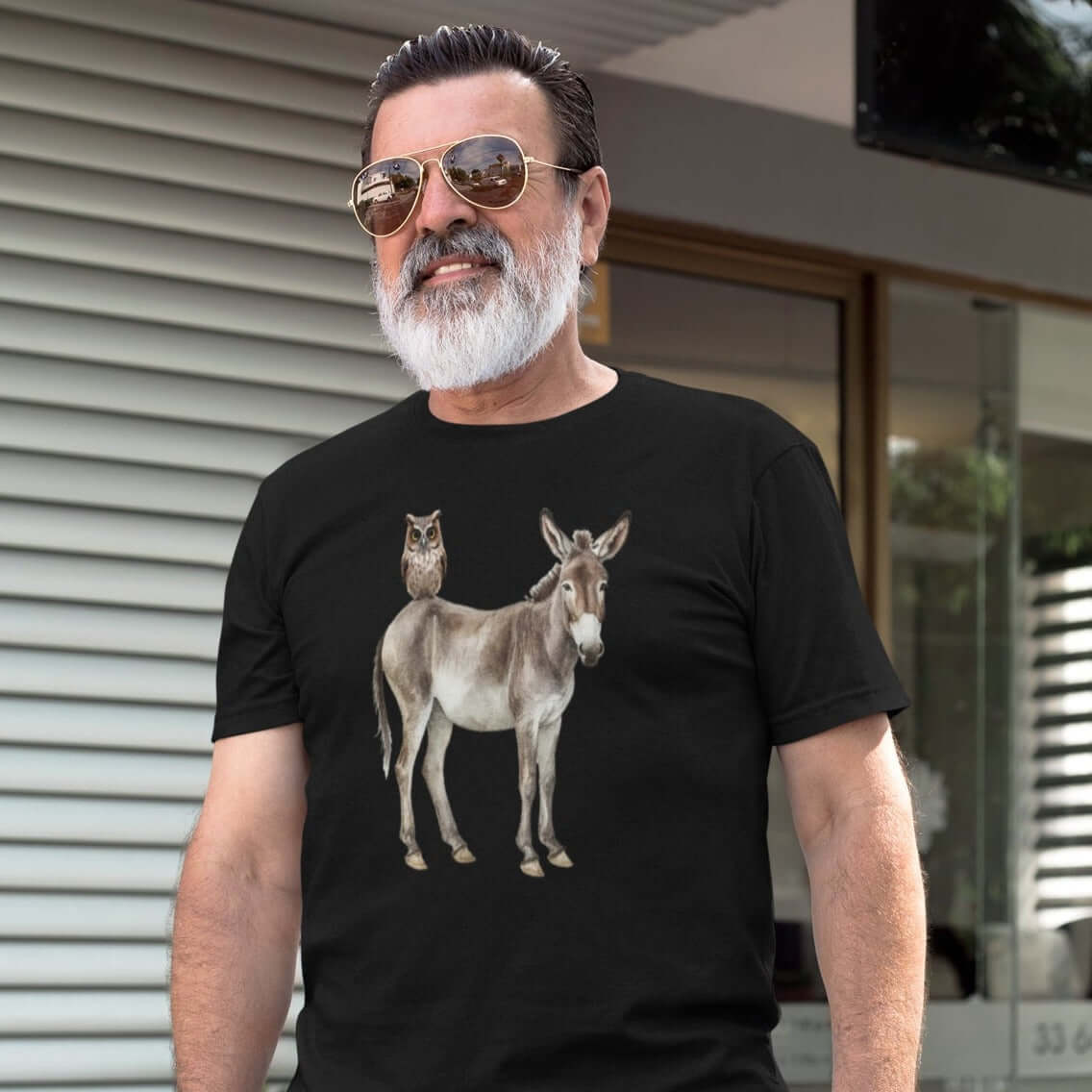 Older man with a beard wearing a black t-shirt with an image of a donkey with wise owl sitting on it printed on the front.