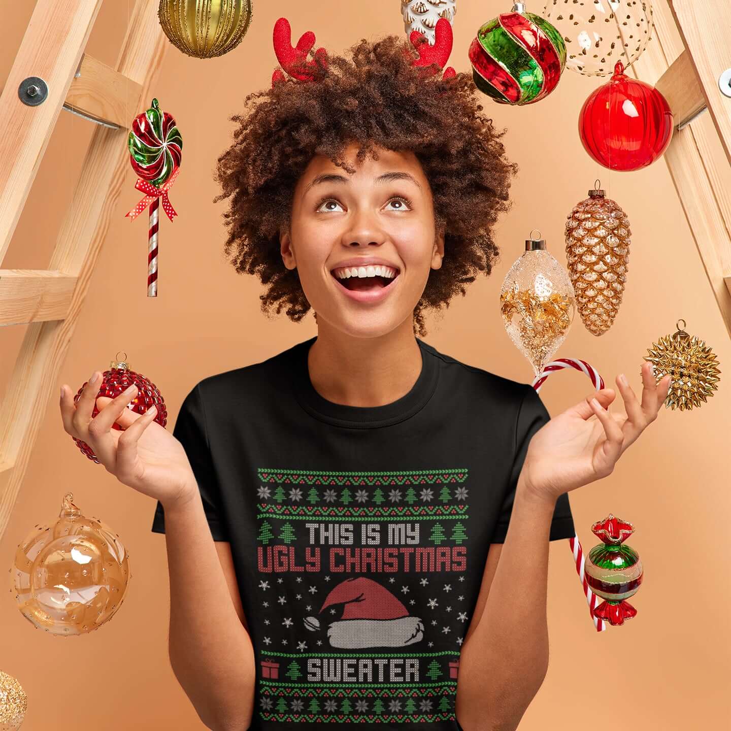 Excited woman in a holiday setting. She is wearing a black t-shirt with the phrase This is my ugly Christmas sweater printed on the front in sweater print font.