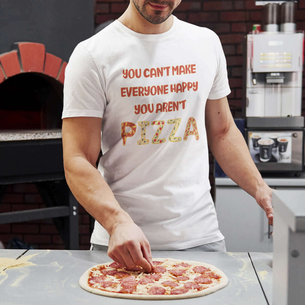 Man making pizza while wearing a white t-shirt with the phrase You can't make everyone happy, you aren't pizza printed on the front.