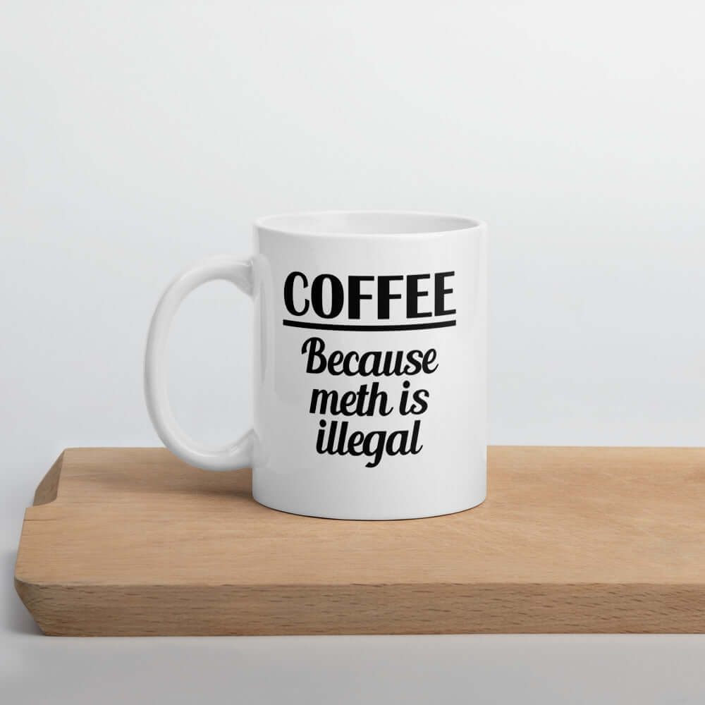 White ceramic coffee mug with the funny phrase Coffee because meth is illegal printed on both sides of the mug.
