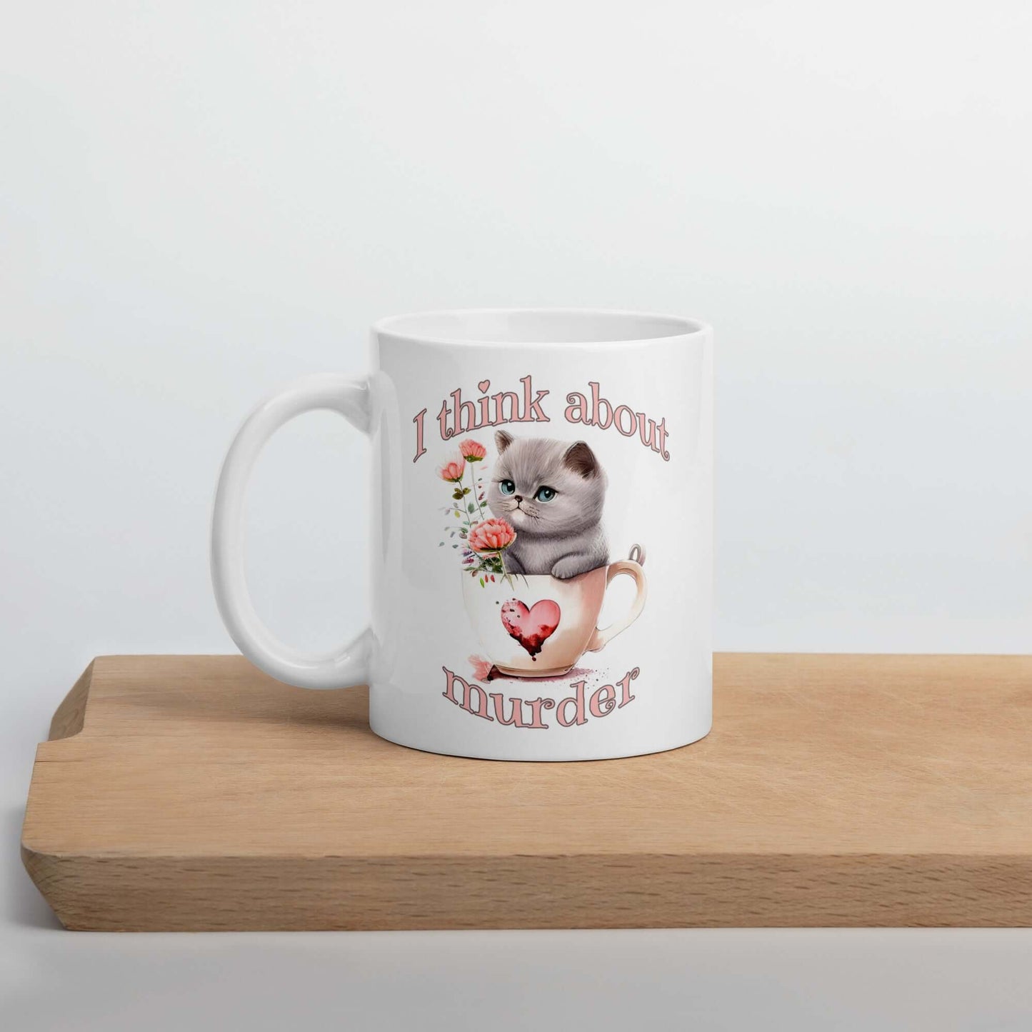 White ceramic mug that says I think about murder with image of cute fluffy kitten sitting in a teacup printed on both sides.