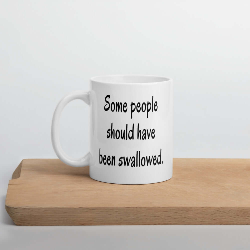White ceramic coffee mug with the phrase some people should have been swallowed printed on both sides.