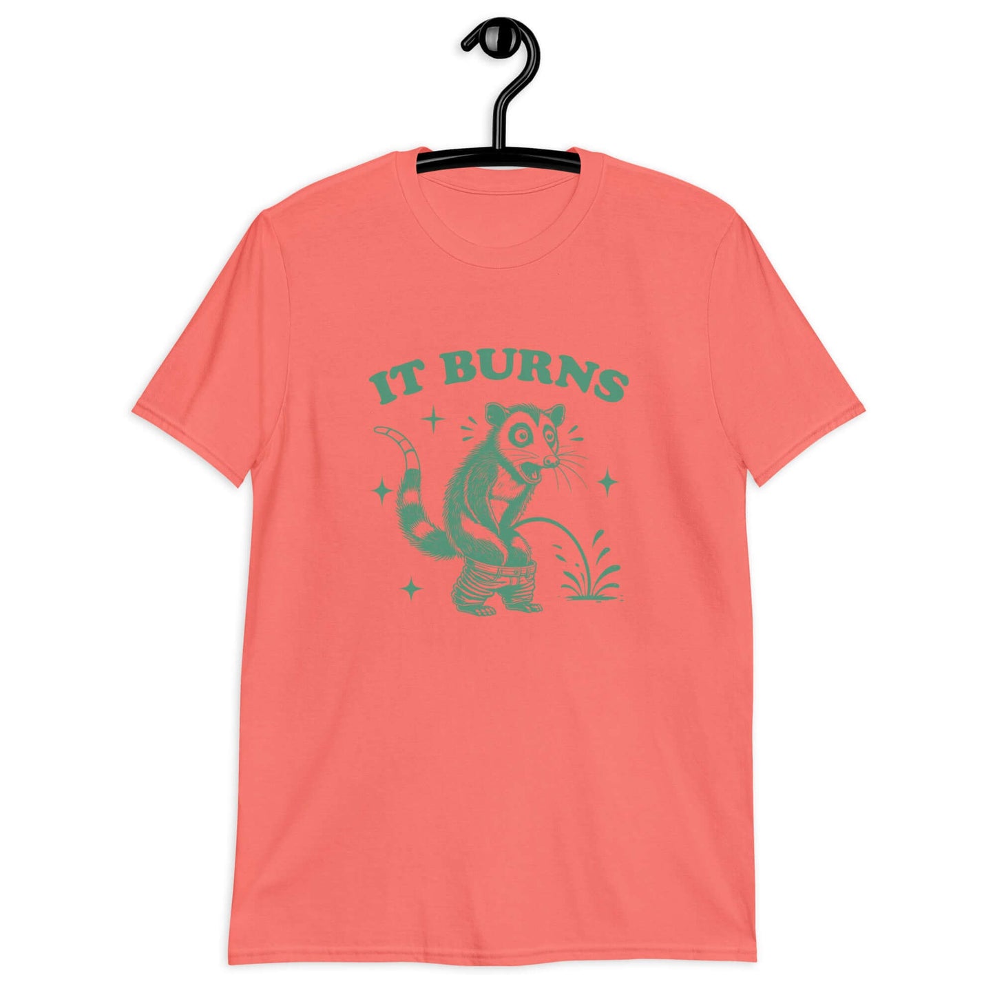 Coral color t-shirt with an image of an opossum peeing. The words It burns are printed above.