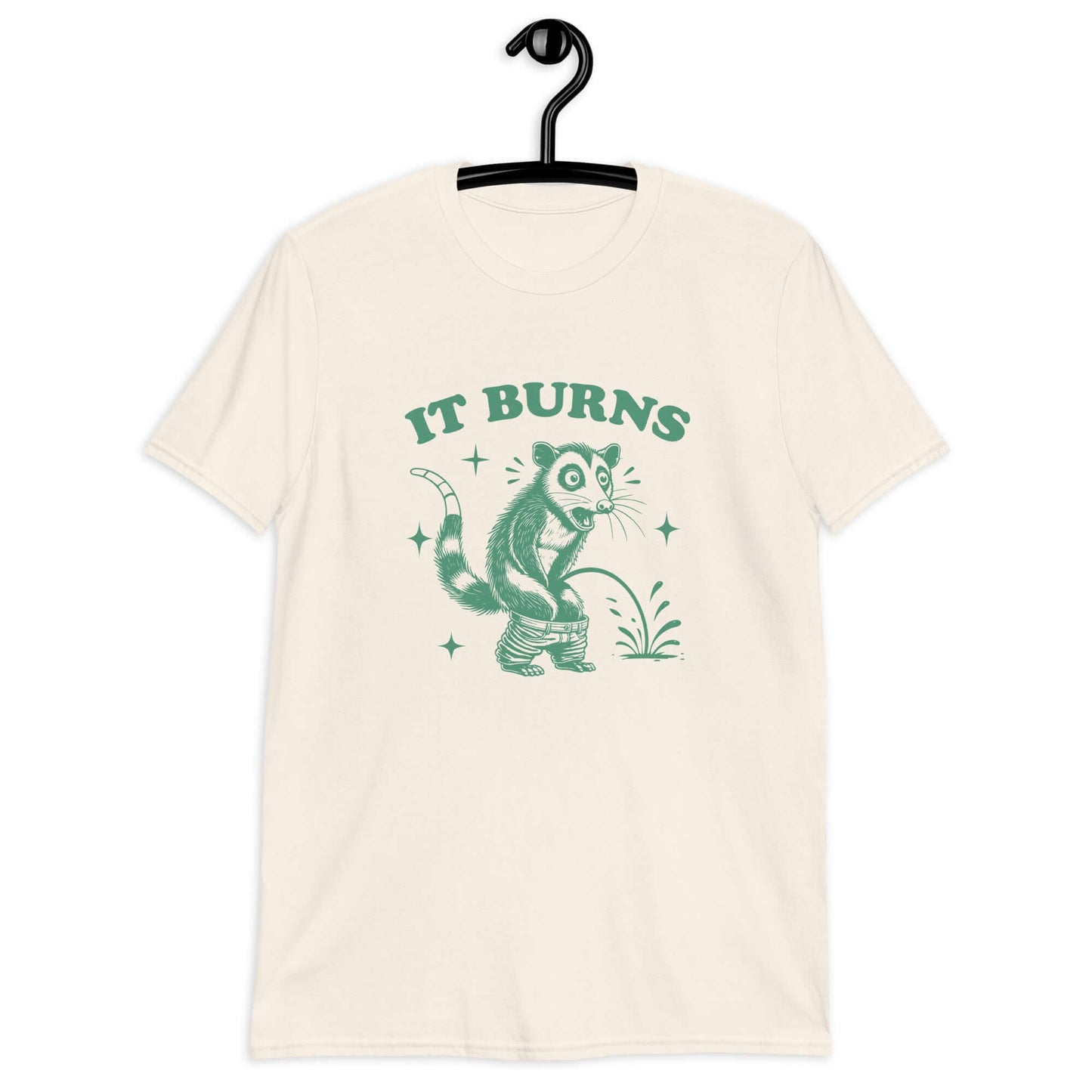 Natural color t-shirt with an image of an opossum peeing. The words It burns are printed above.
