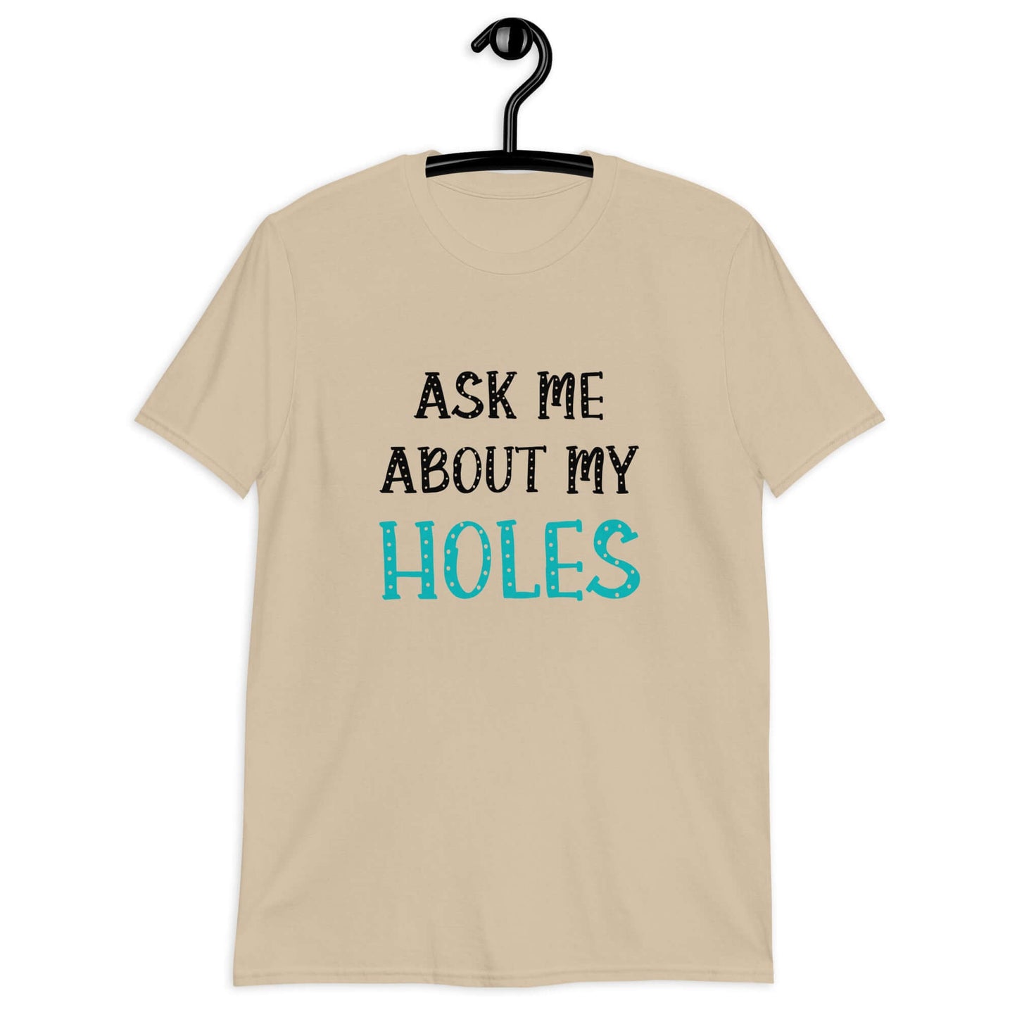 Sand color t-shirt with the words Ask me about my holes printed on the front. The word holes in turquoise color and the rest of the text is black.