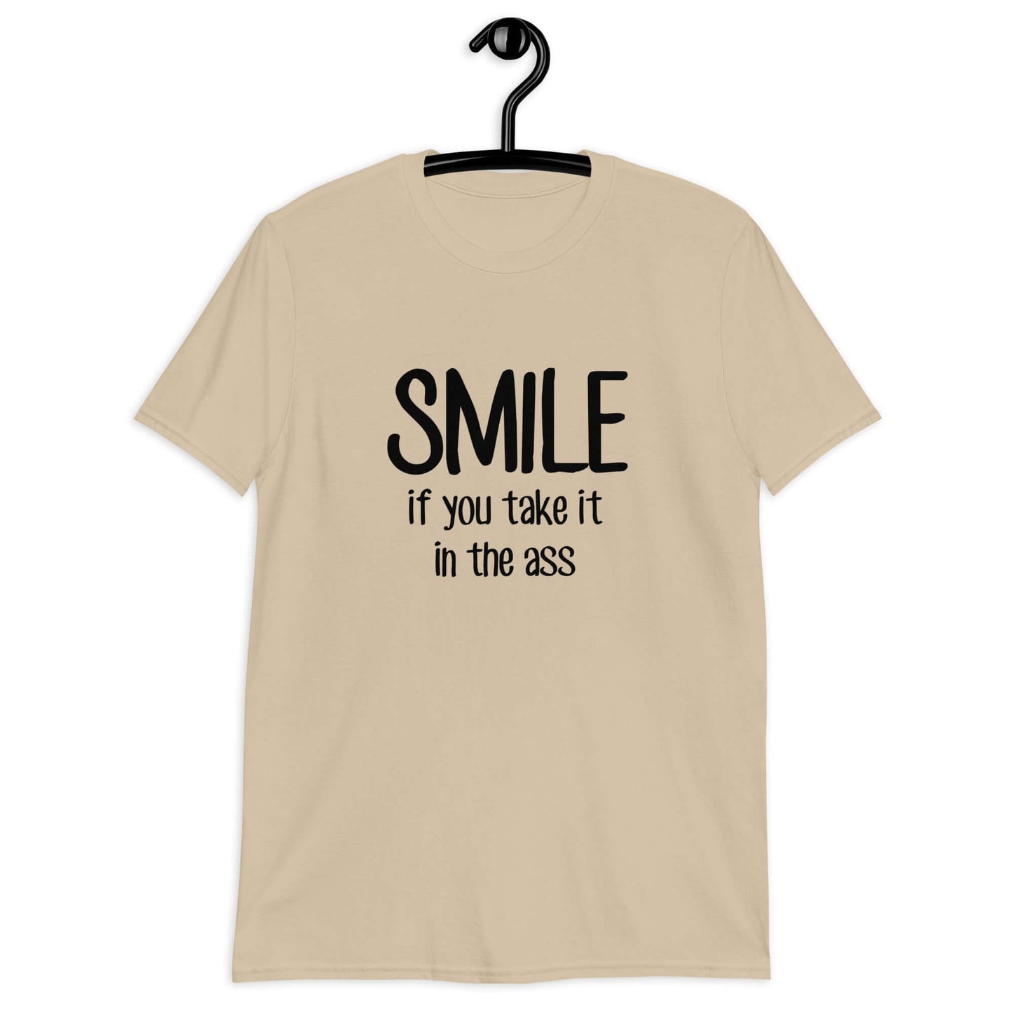 Sand color t-shirt with the phrase Smile if you take it in the ass printed on the front. The word smile is large and the words take it in the ass are much smaller.