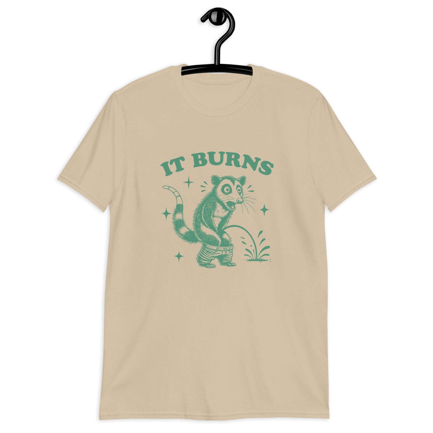 Sand color t-shirt with an image of an opossum peeing. The words It burns are printed above.