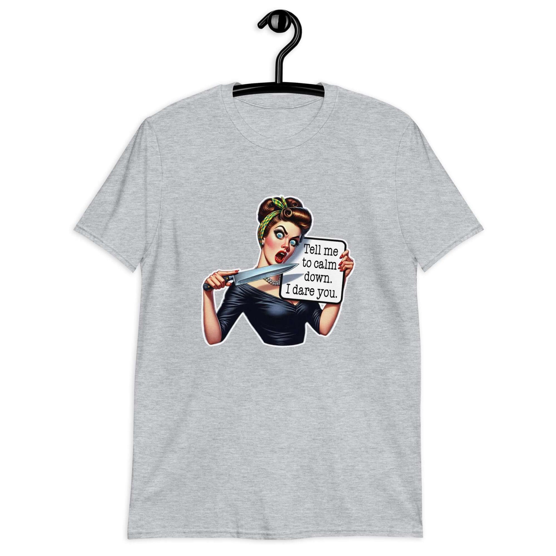Sport grey t-shirt displayed on a hanger. The t-shirt has a graphic of an angry looking retro woman holding a knife and a sign. The sign says Tell me to calm down I dare you. The graphic is printed on the front of the shirt.