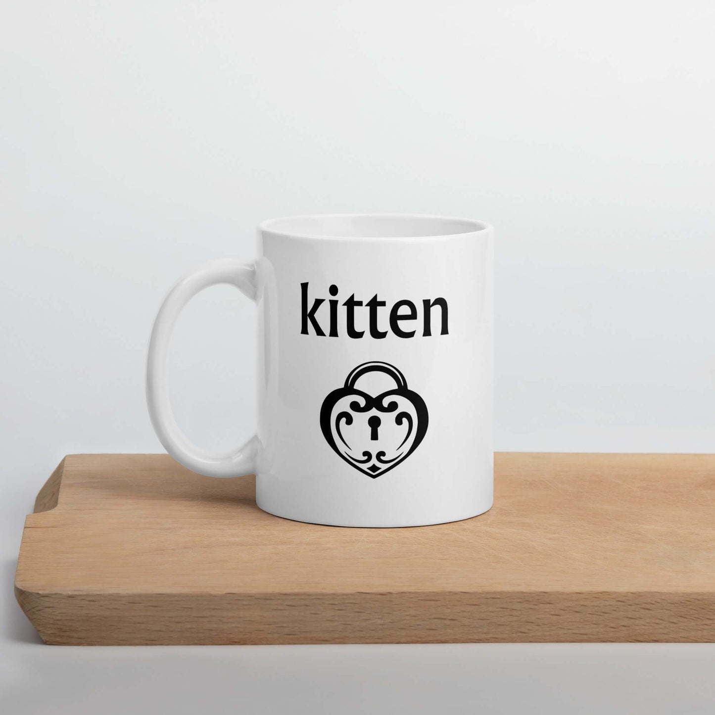 White ceramic coffee mug with an image of a heart shaped lock and the word kitten printed on both sides of the mug.
