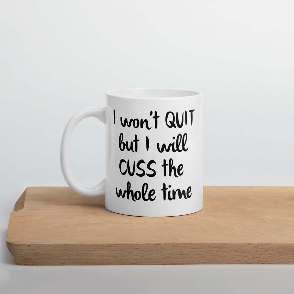 White ceramic mug with the phrase I won't quit but I will cuss the whole time printed on both sides of the mug.
