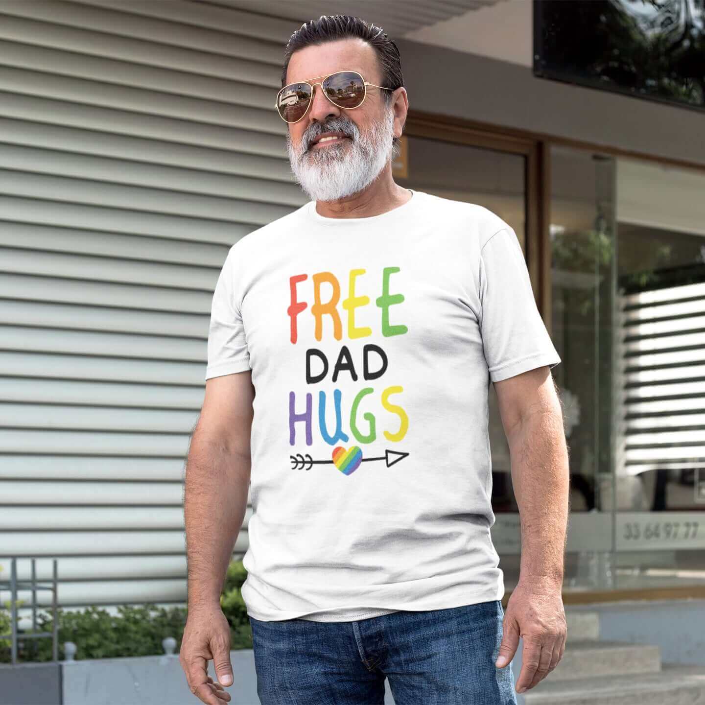 Older bearded man wearing white t-shirt with the words Free Dad hugs printed on the front in rainbow letters.
