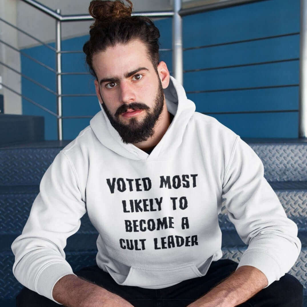 Serious looking man wearing a white hooded sweatshirt with the words Voted most likely to become a cult leader printed on the front.