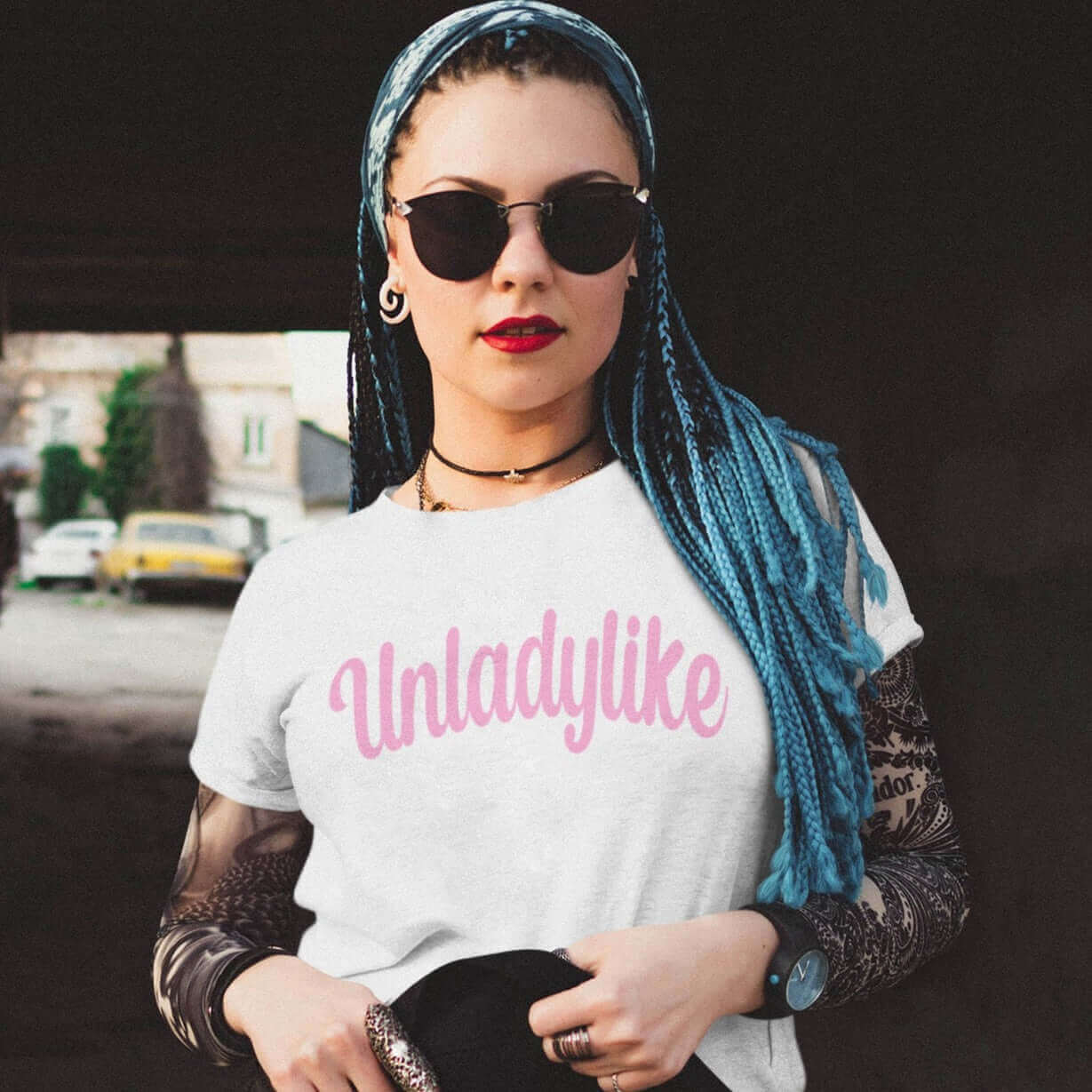 Woman wearing sunglasses and a white t-shirt with the word Unladylike printed on the front in pink.