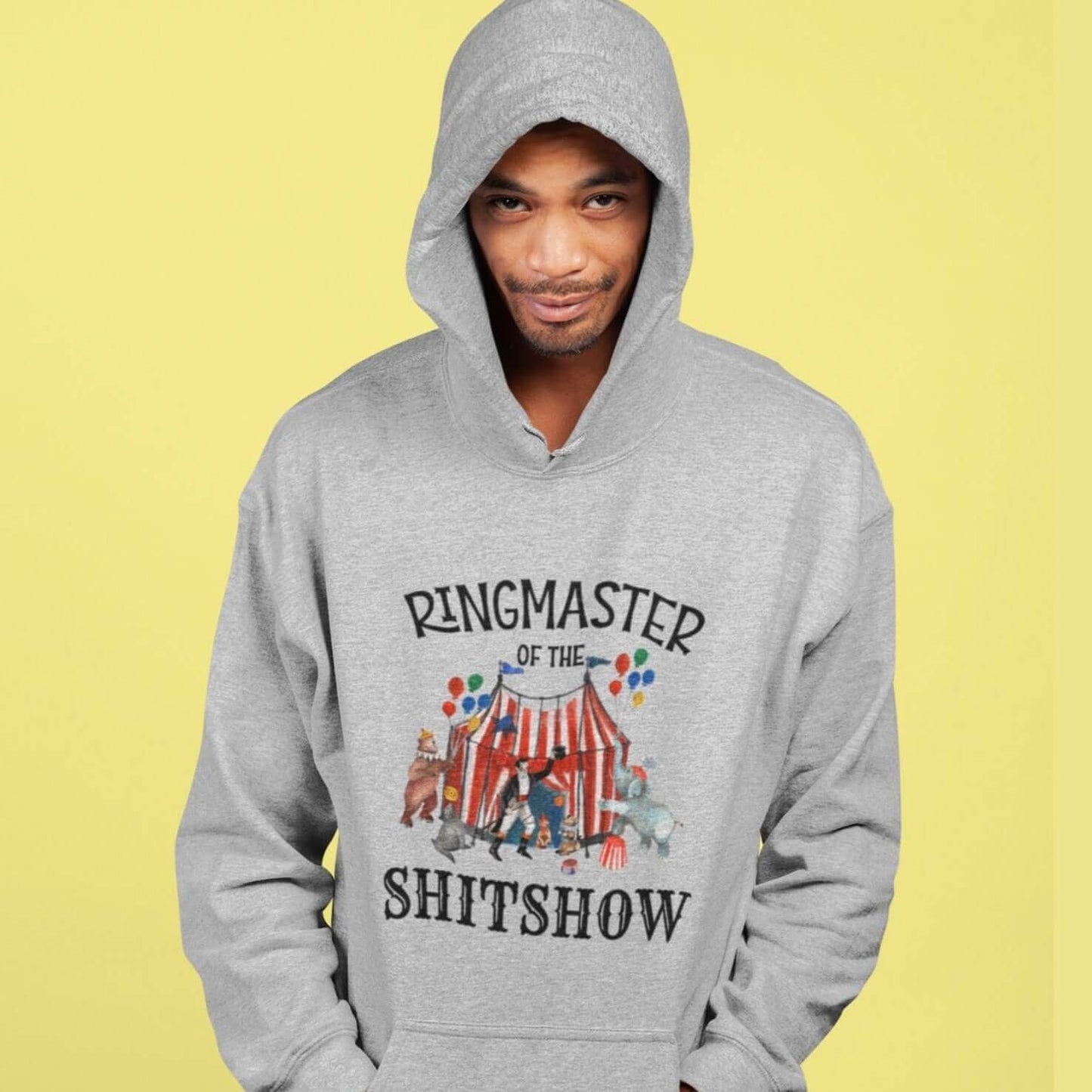 Man wearing a light grey hoodie sweatshirt with a circus theme graphic and the words Ringmaster of the Shitshow printed on the front.