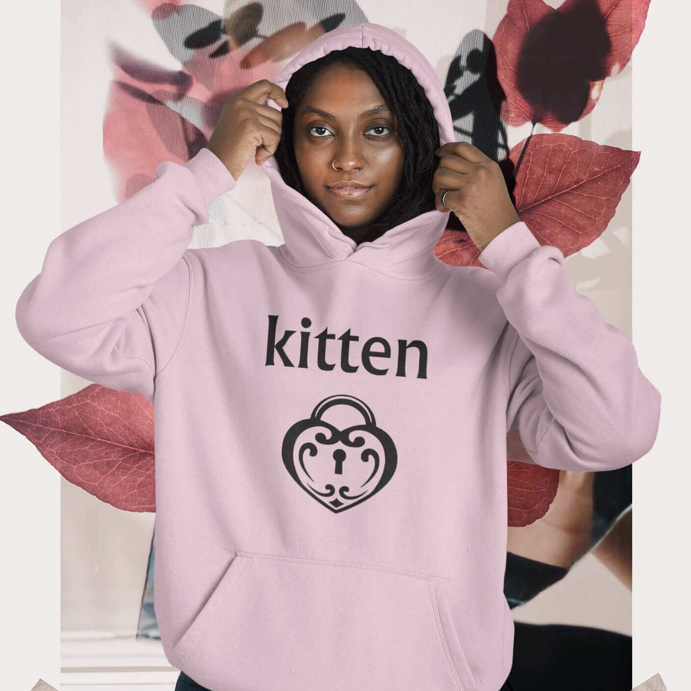 Woman wearing a light pink hoodie sweatshirt with an image of a heart shaped lock and the word kitten printed on the front.