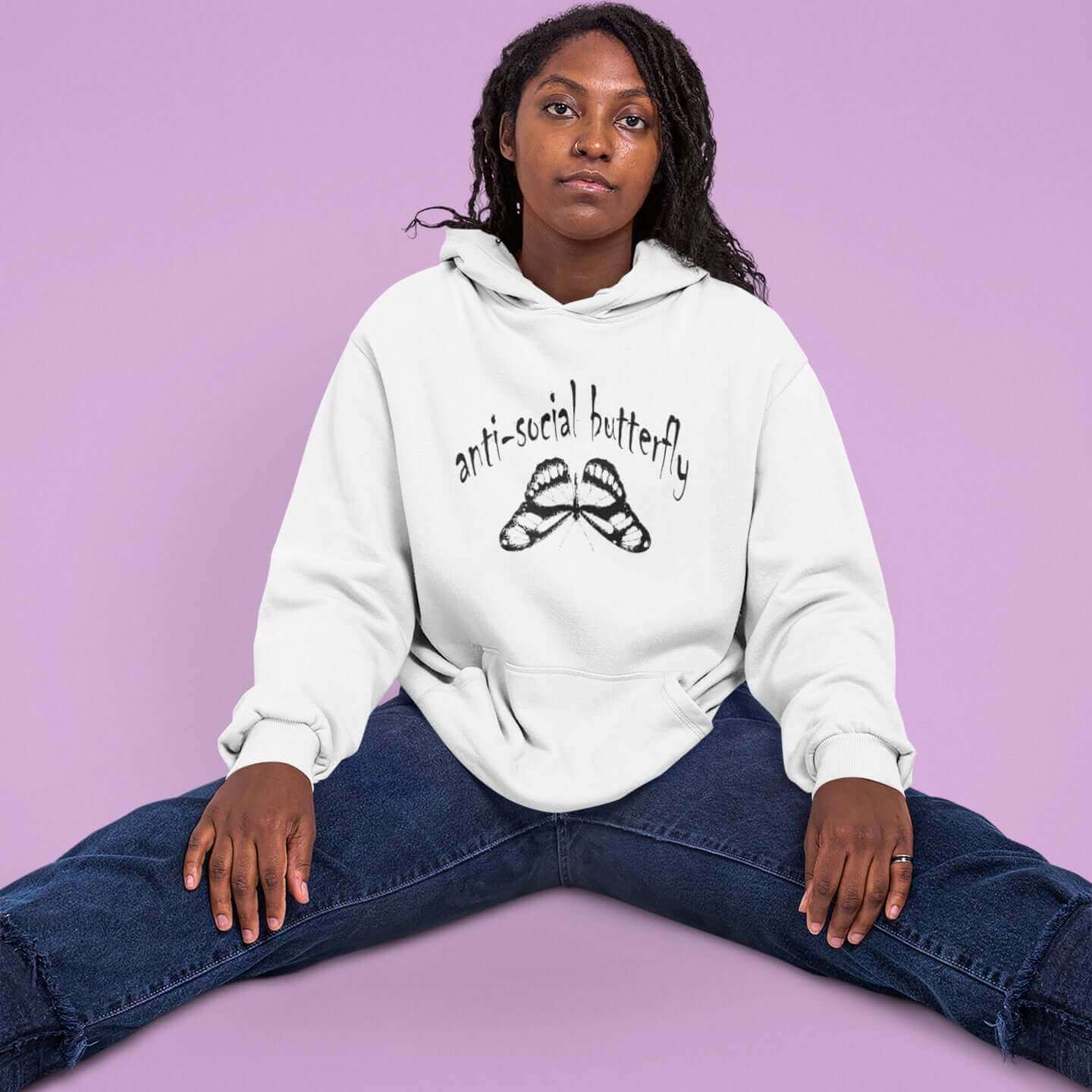 Woman sitting on the floor wearing a white hoodie sweatshirt. The hoodie has an image of an upside down butterfly and the words Anti-social butterfly printed on the front.