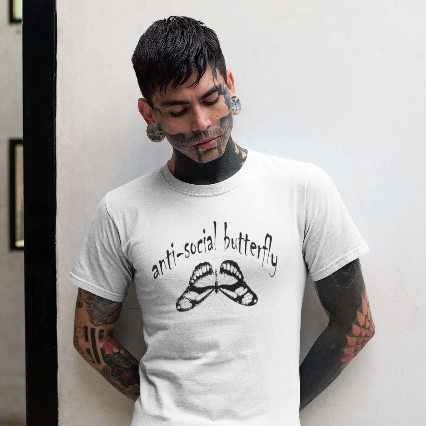 Tattooed man wearing a white t-shirt with an image of an upside down butterfly and the words Anti-social butterfly printed on the front.