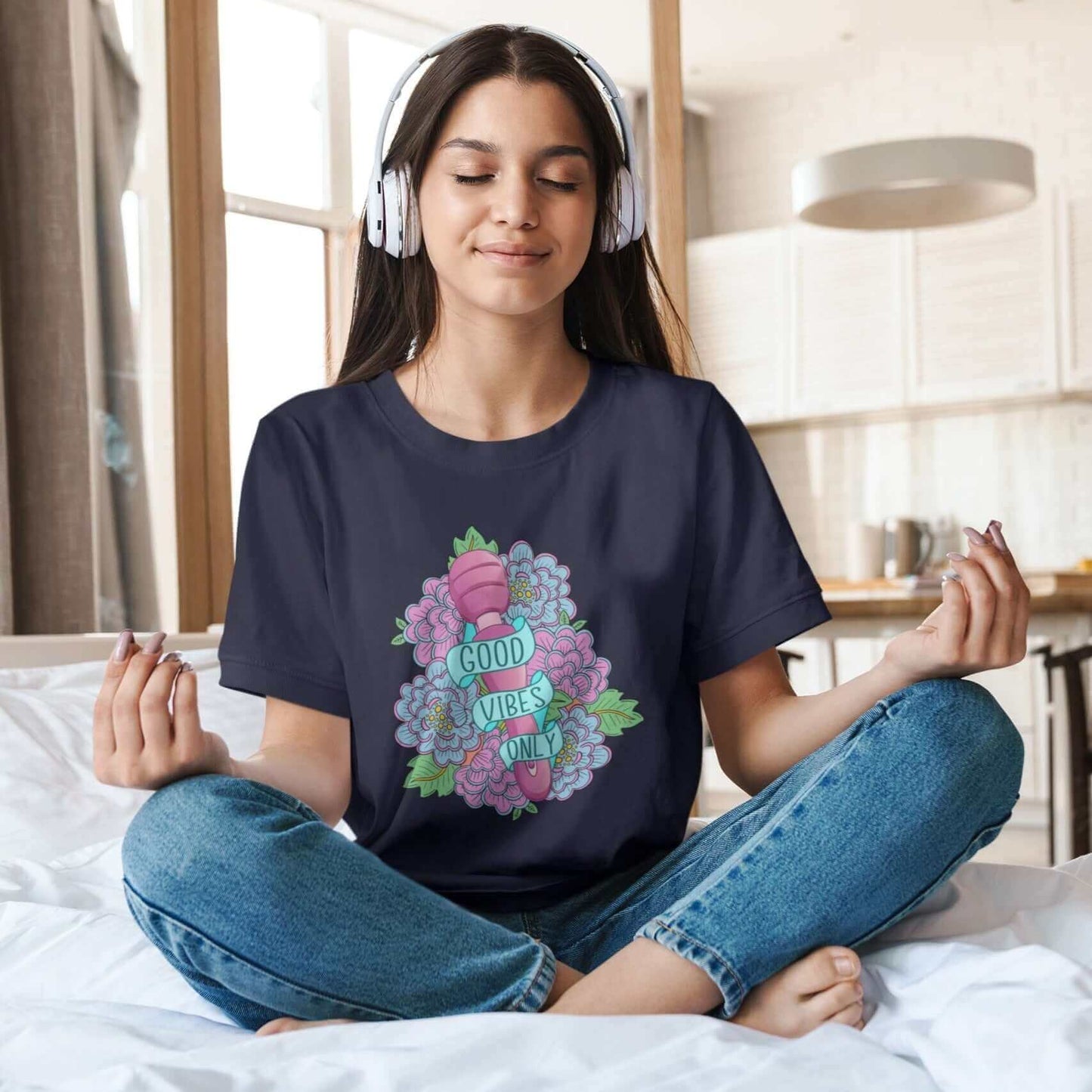 Woman meditating wearing navy blue t-shirt with graphic design that has the words Good vibes only layered over a pink wand vibrator with flowers around. The graphic design is printed on the front of the shirt.