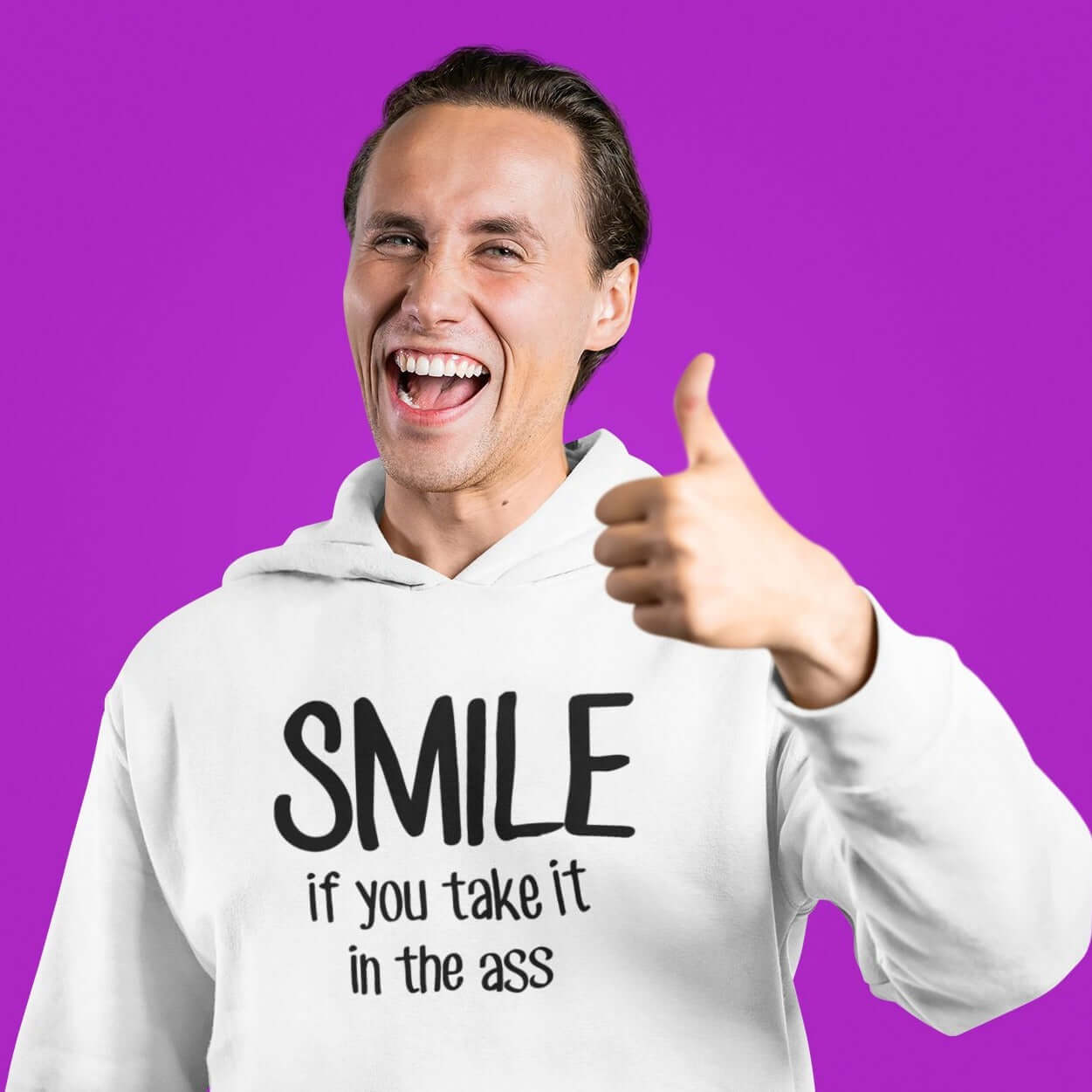 Man giving a thumbs up sign while wearing a white hoodie sweatshirt. The hoodie has the phrase Smile if you take it in the ass printed on the front. The word smile is large and the words take it in the ass are much smaller.