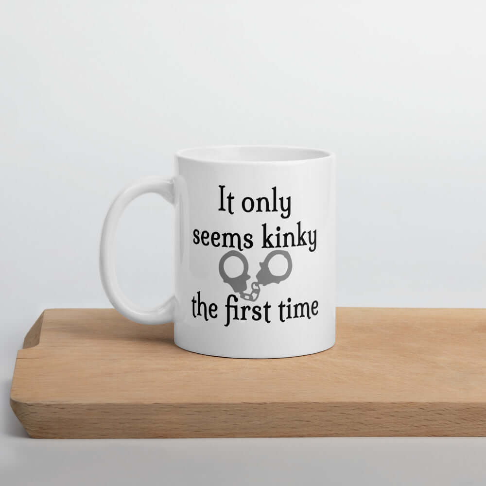 White ceramic coffee mug with the phrase It only seems kinky the first time printed on both sides of the mug. There is an image of handcuffs with the text.