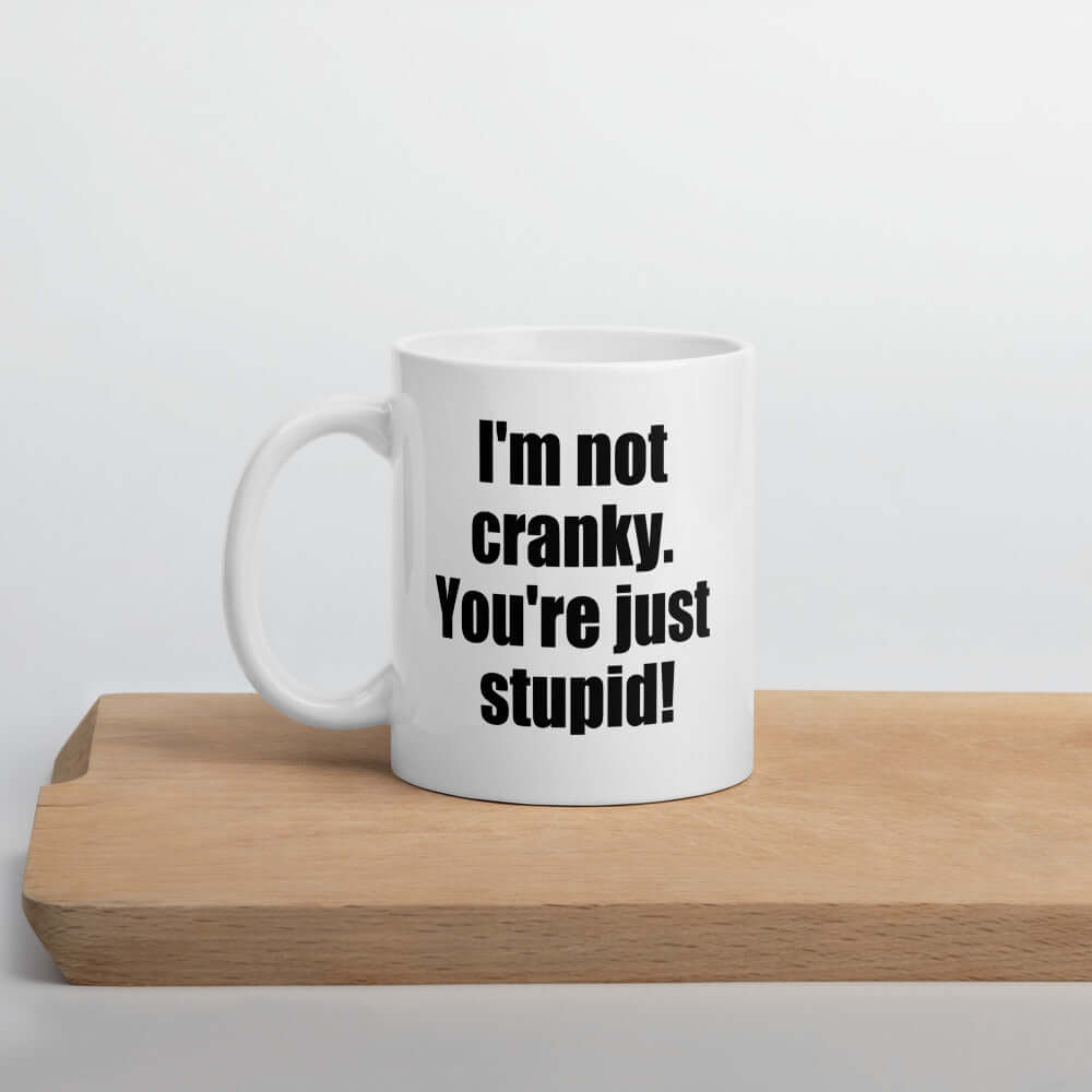 White ceramic coffee mug with the phrase I'm not cranky You're just stupid printed on both sides of the mug.