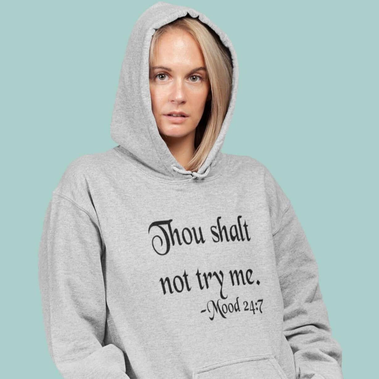 Woman wearing a light grey hoodie sweatshirt with the mock scripture quote Thou shalt not try me Mood 24:7 printed on the front.