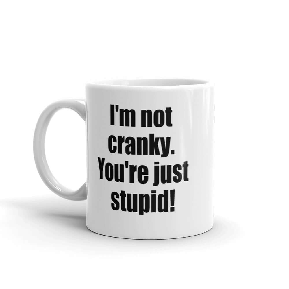 White ceramic coffee mug with the phrase I'm not cranky You're just stupid printed on both sides of the mug.