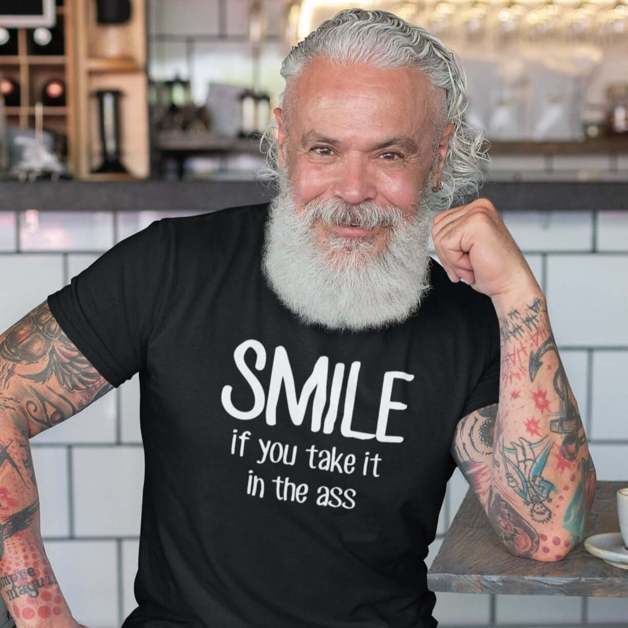Handsome grinning man wearing a black t-shirt with the phrase Smile if you take it in the ass printed on the front. The word smile is large and the words take it in the ass are much smaller.