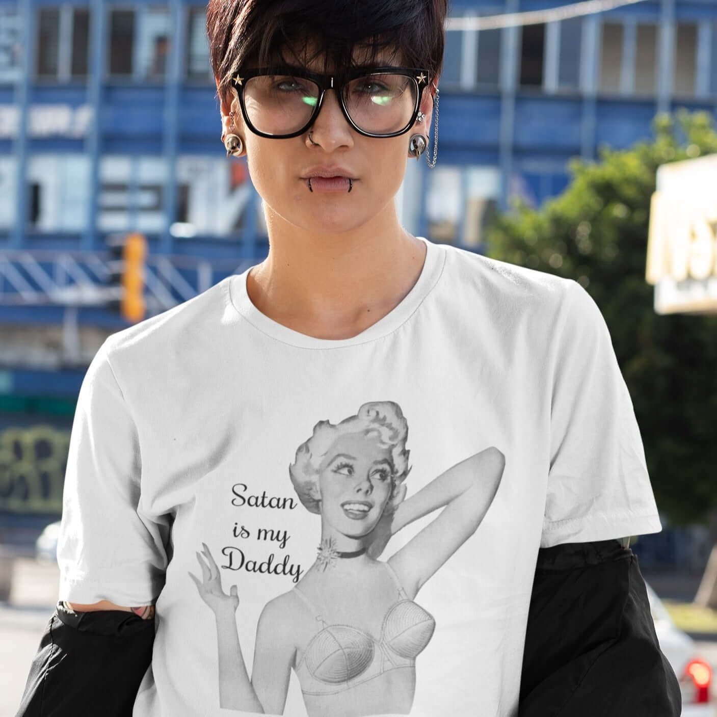 Edgy looking woman wearing a white t-shirt with image of a retro black & white pin-up model and the phrase Satan is my Daddy printed on the front.