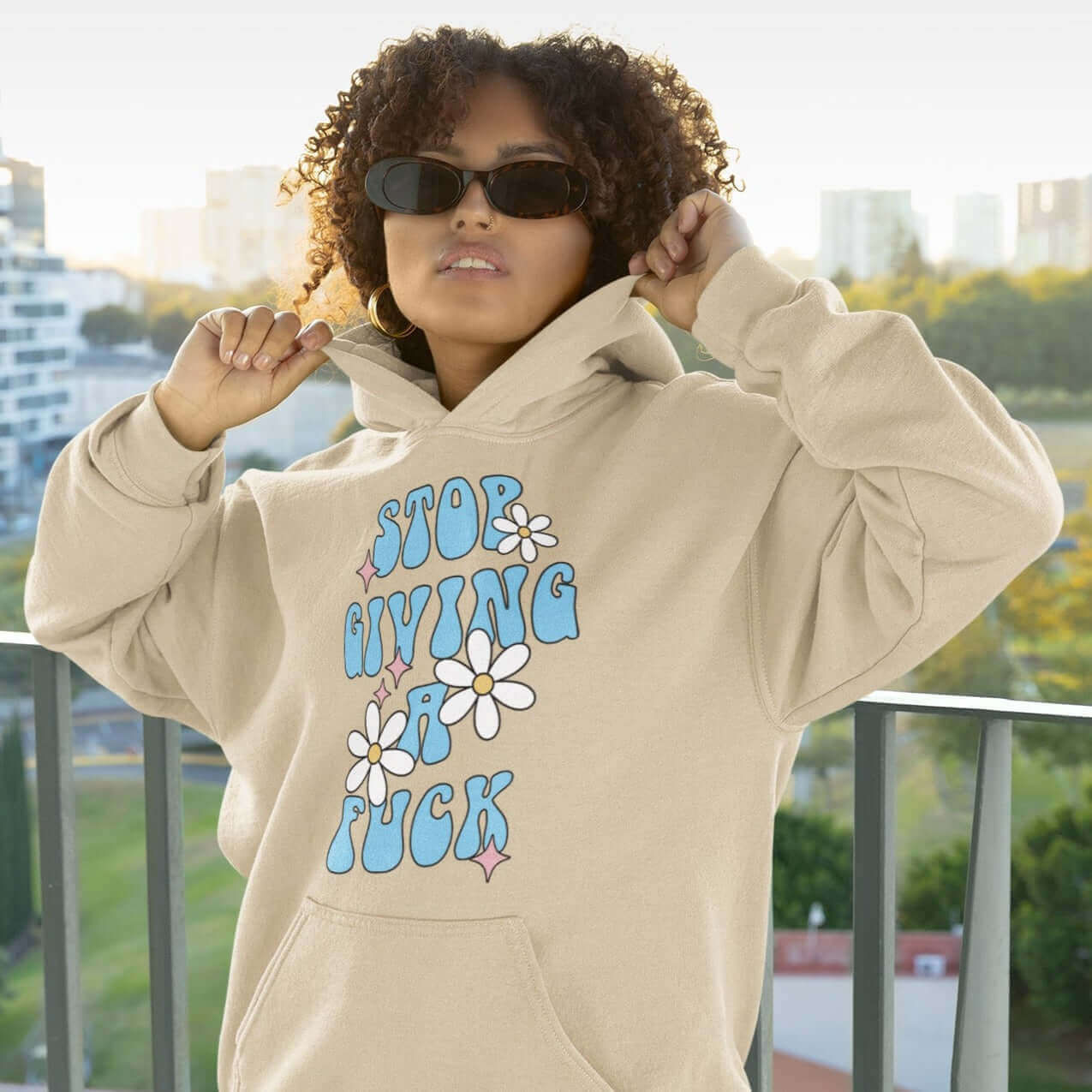 Woman wearing sand color hoodie sweatshirt with stop giving a fuck printed on the front.