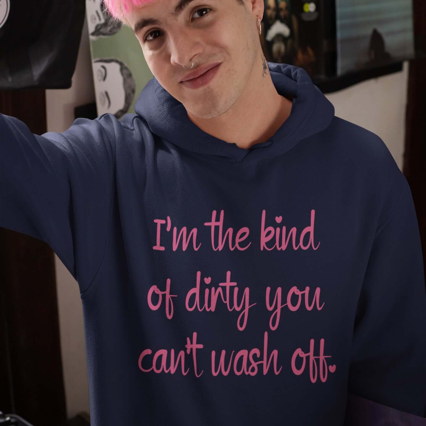 Man with pink hair wearing a navy blue hoodie sweatshirt with the words I'm the kind of dirty you can't wash off printed on the front of the hoodie. The text is pink.