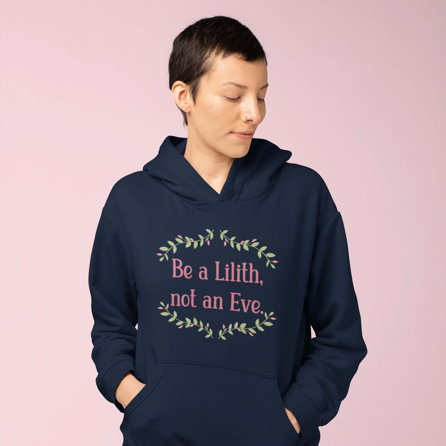 Woman wearing a navy blue hoodie sweatshirt with the phrase Be a Lilith, not an Eve printed on the front. The text is pink and had a green floral vine graphic framing the text. 