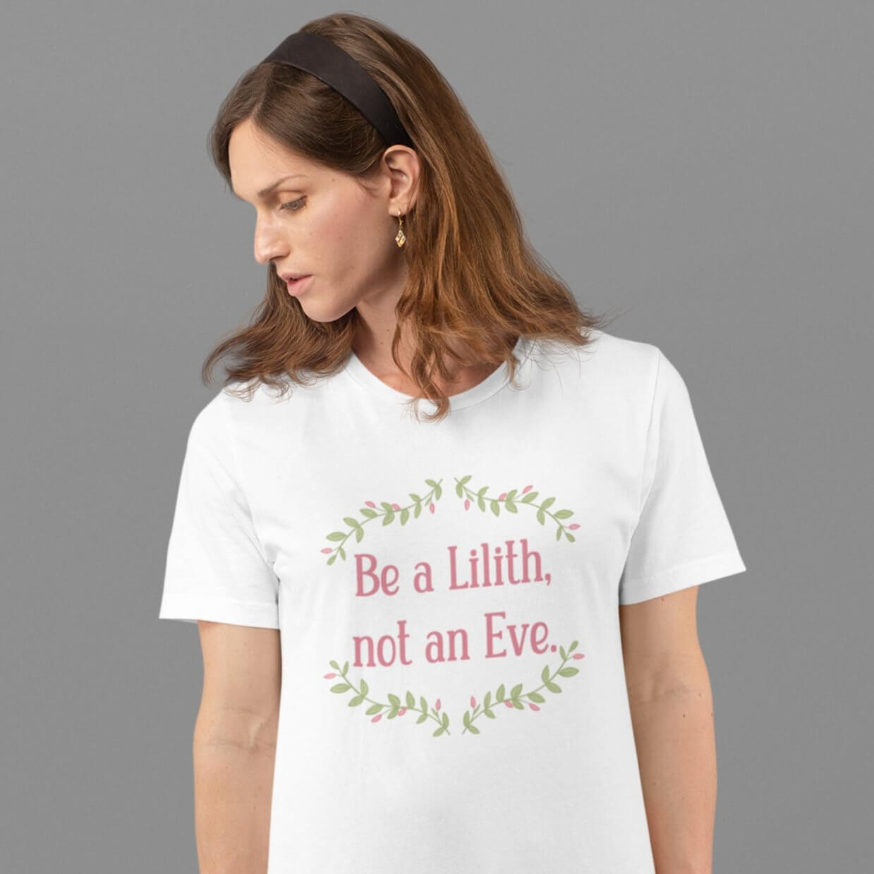 Woman wearing a white t-shirt with the phrase Be a Lilith, not an Eve printed on the front. The text is pink and had a green floral vine graphic framing the text. 