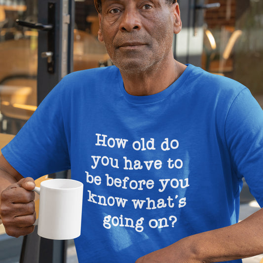 Older man wearing a royal blue t-shirt with the phrase How old do you have to be before you know whats going on question mark printed on the front.