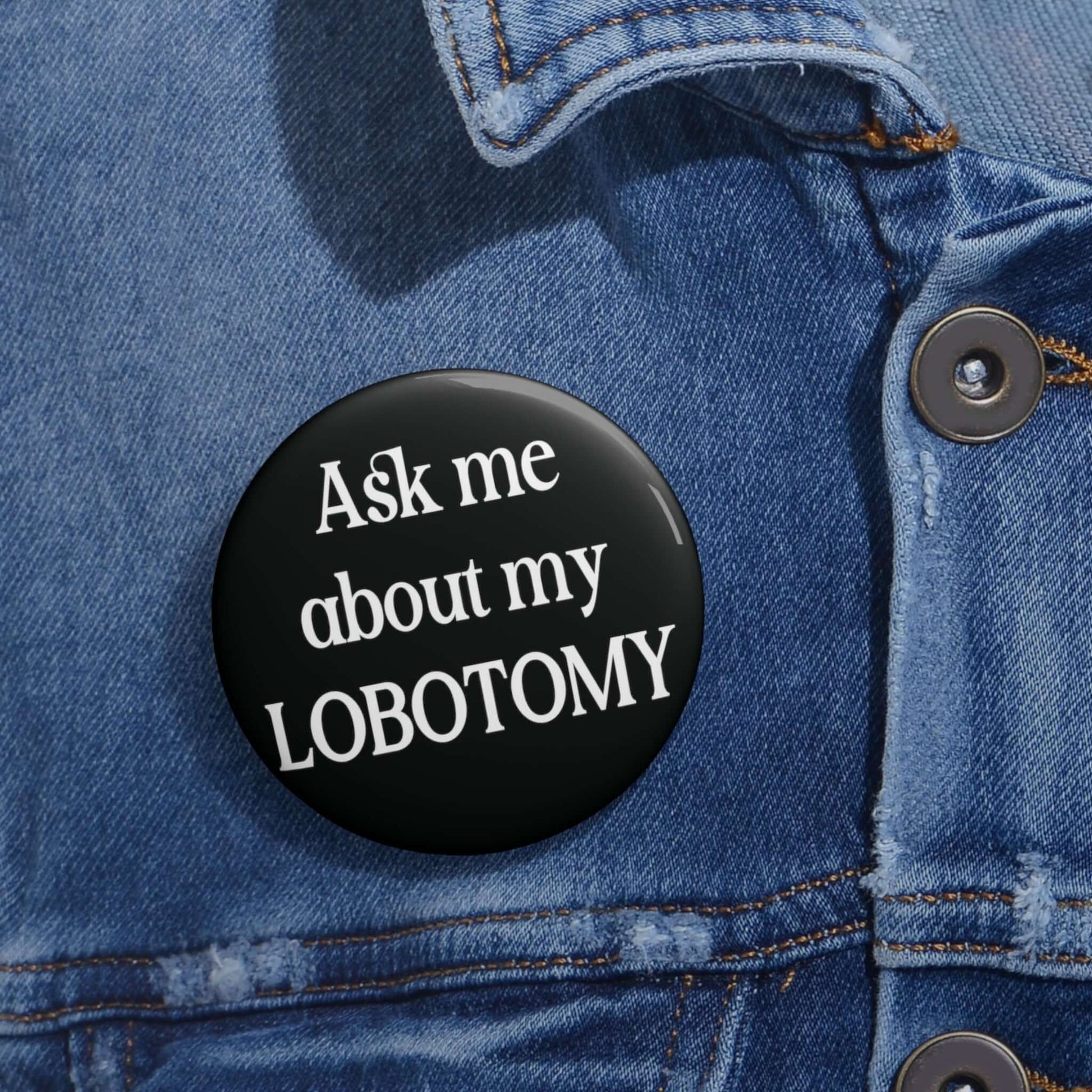 Black pin-back button with the phrase Ask me about my lobotomy printed on it.