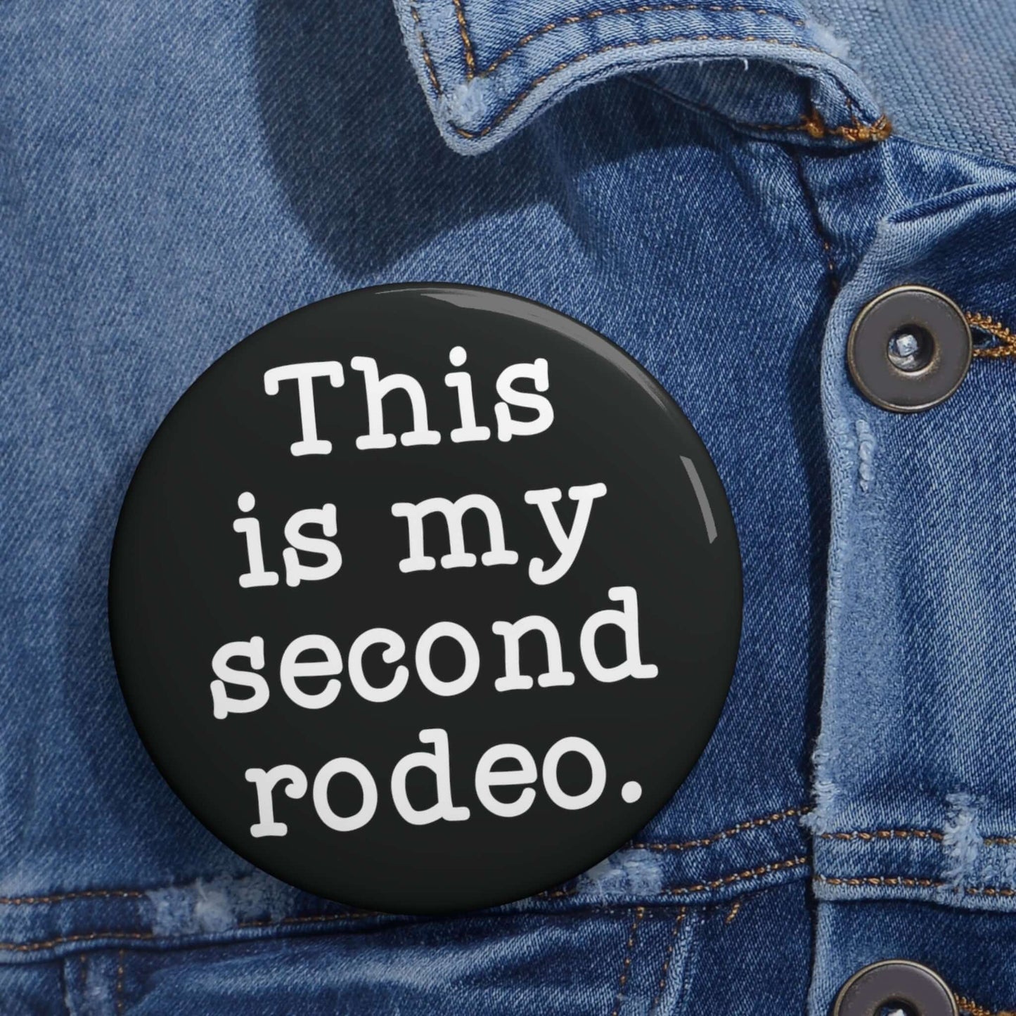 Black pin-back button with the phrase This is my second rodeo printed on it in white.