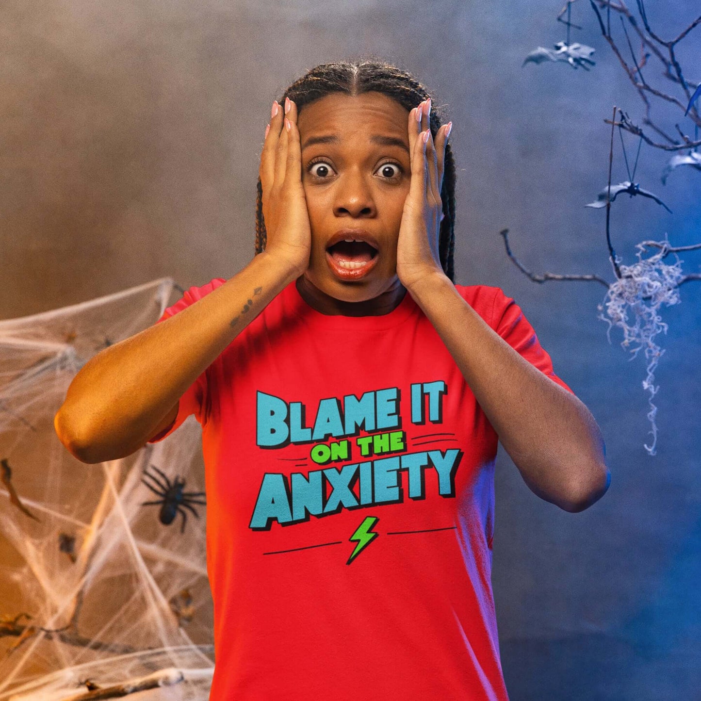 Freaked out woman wearing a red t-shirt with the phrase Blame is on the anxiety printed on the front. The graphics are bold and in aqua and lime green.