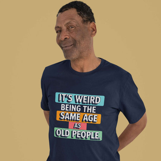 Older man wearing a navy blue t-shirt with colorful graphics that say It's weird being the same age as old people printed on the front.