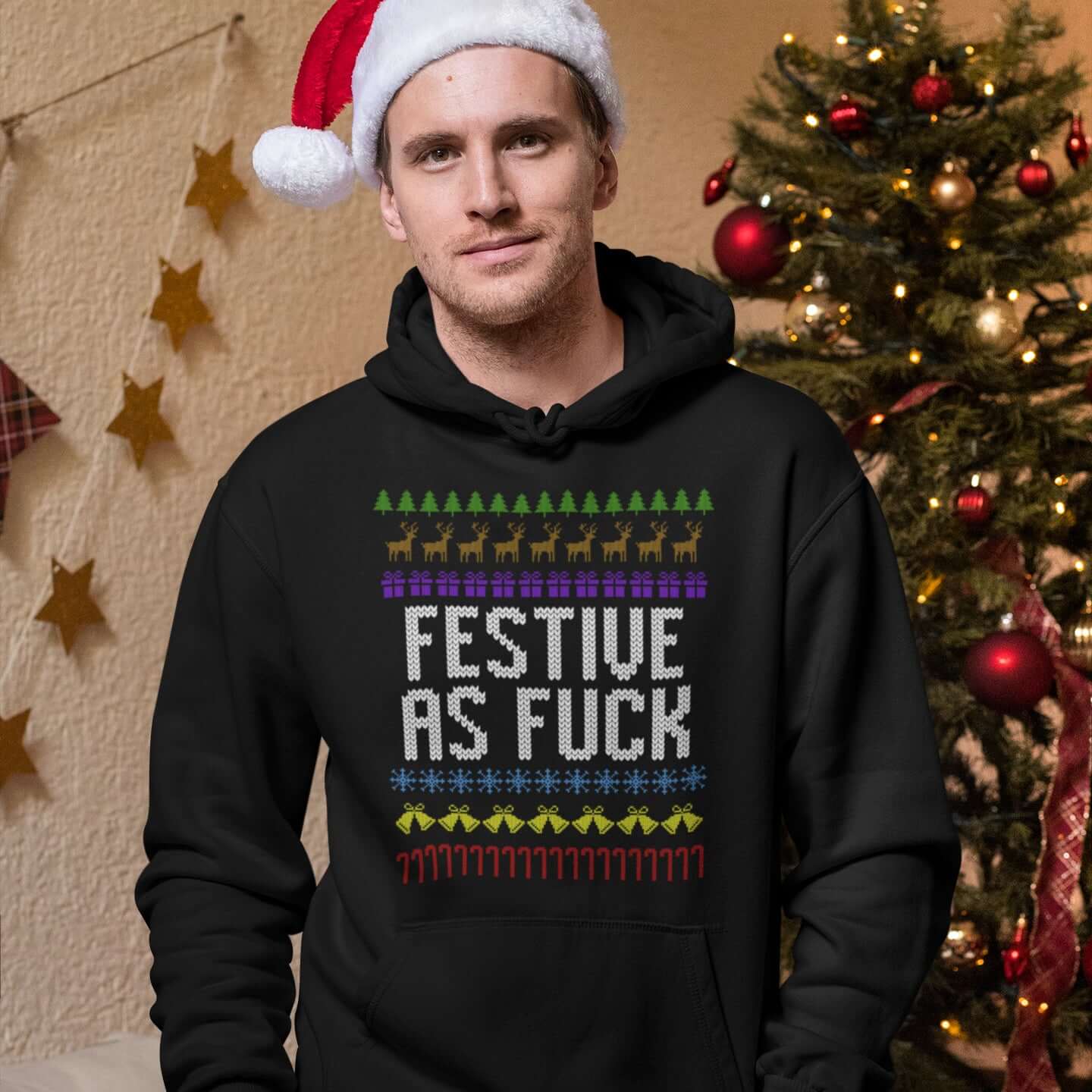 Man wearing a black hoodie sweatshirt with an ugly Christmas sweater design with the phrase Festive as fuck printed on the front.
