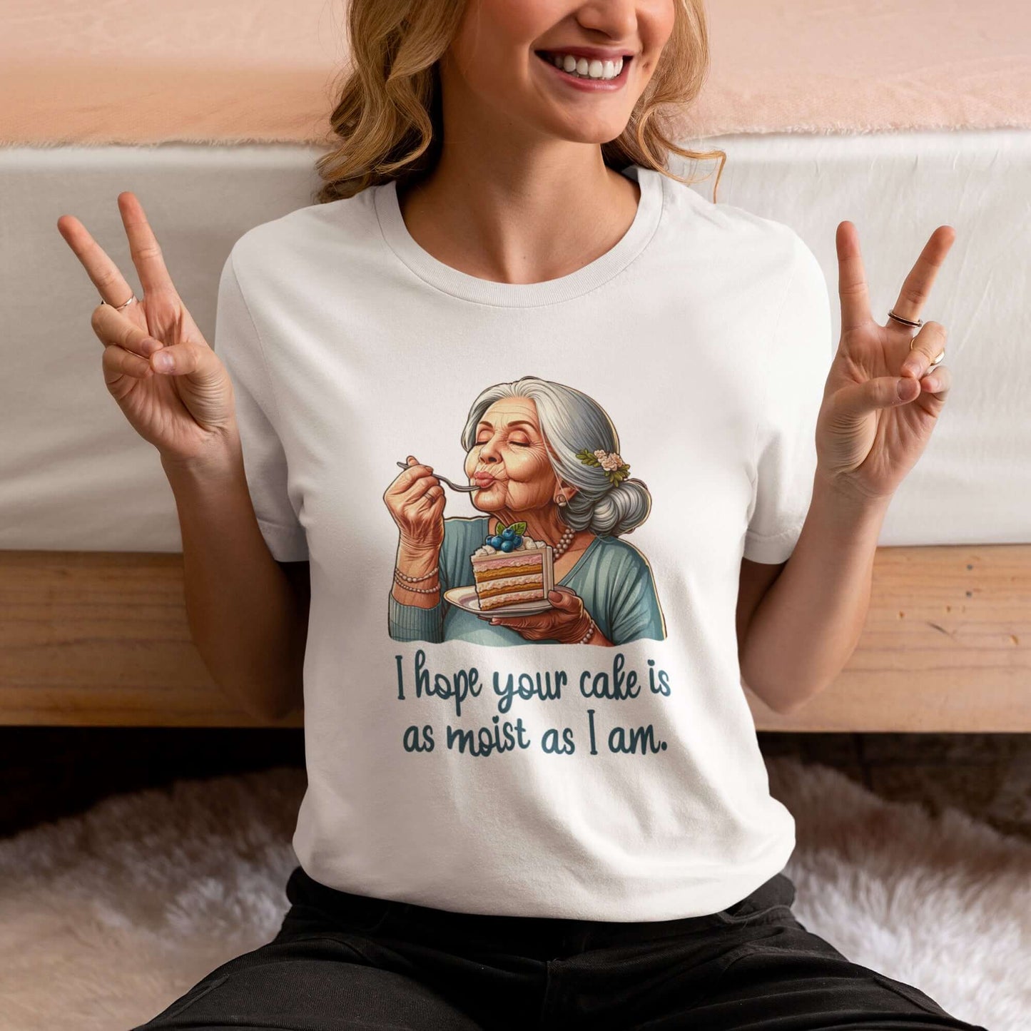 Woman wearing a white t-shirt with image of grey haired older woman enjoying a bite of a piece of cake with the words I hope your cake is as moist as I am printed on the front.