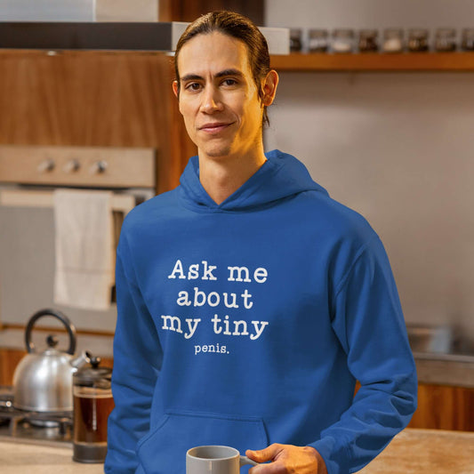 Man wearing a royal blue hoodie sweatshirt with the phrase Ask me about my tiny penis printed on the front. The word tiny is much smaller than the rest of the text.
