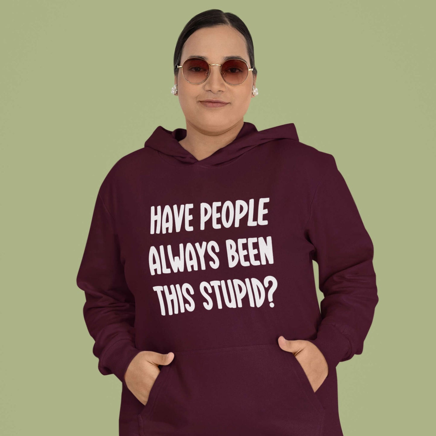 Woman wearing a maroon hoodie sweatshirt with the question Have people always been this stupid question mark printed on the front.