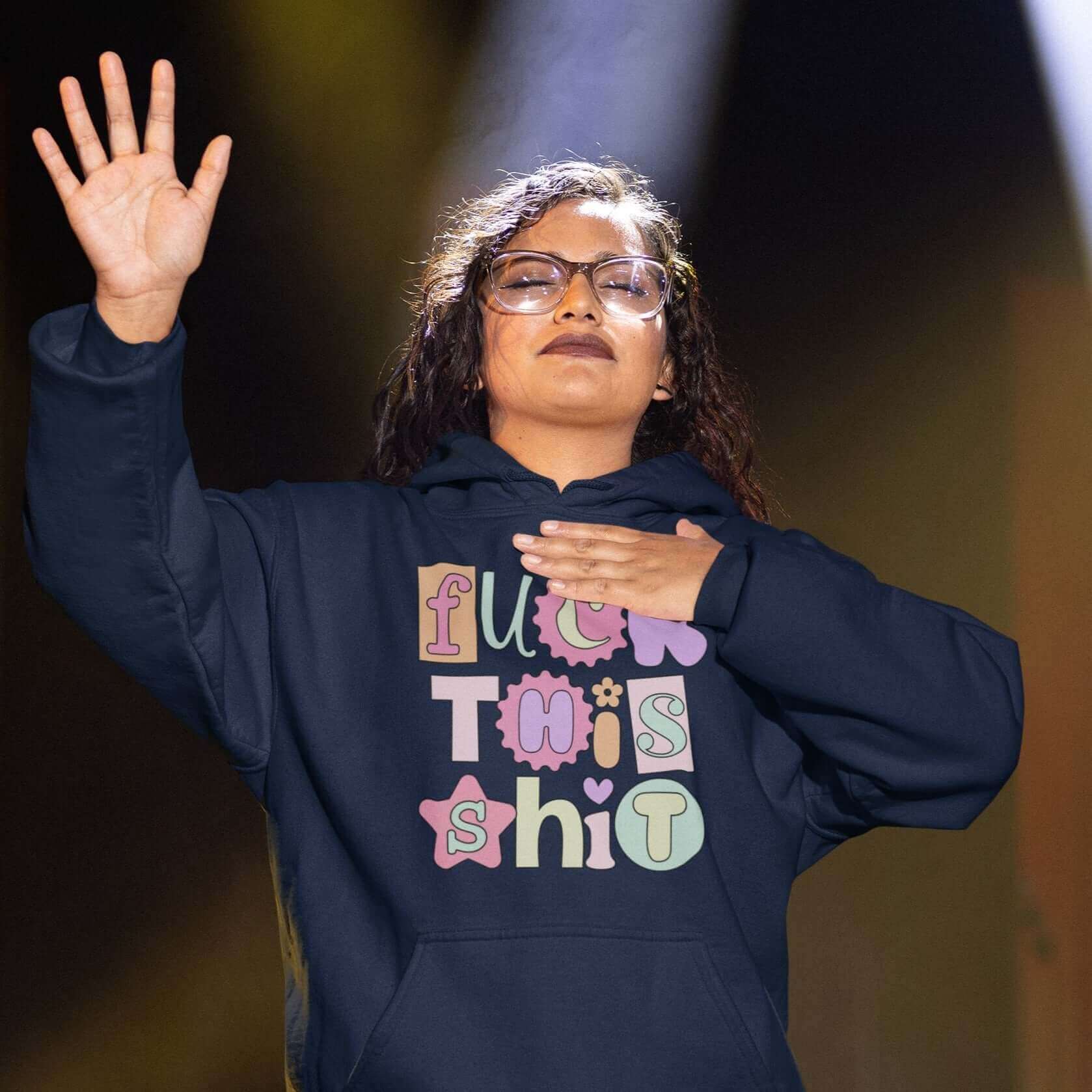 Woman worshiping while wearing navy blue hoodie sweatshirt with colorful font Fuck this shit graphics printed on the front.