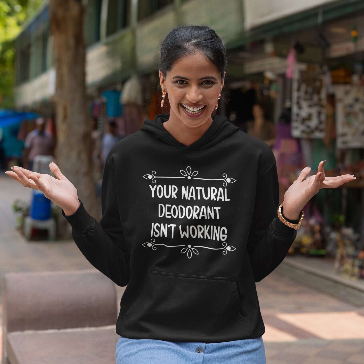 Woman wearing a black hoodie sweatshirt with the funny phrase Your natural deodorant isnt working printed on the front.