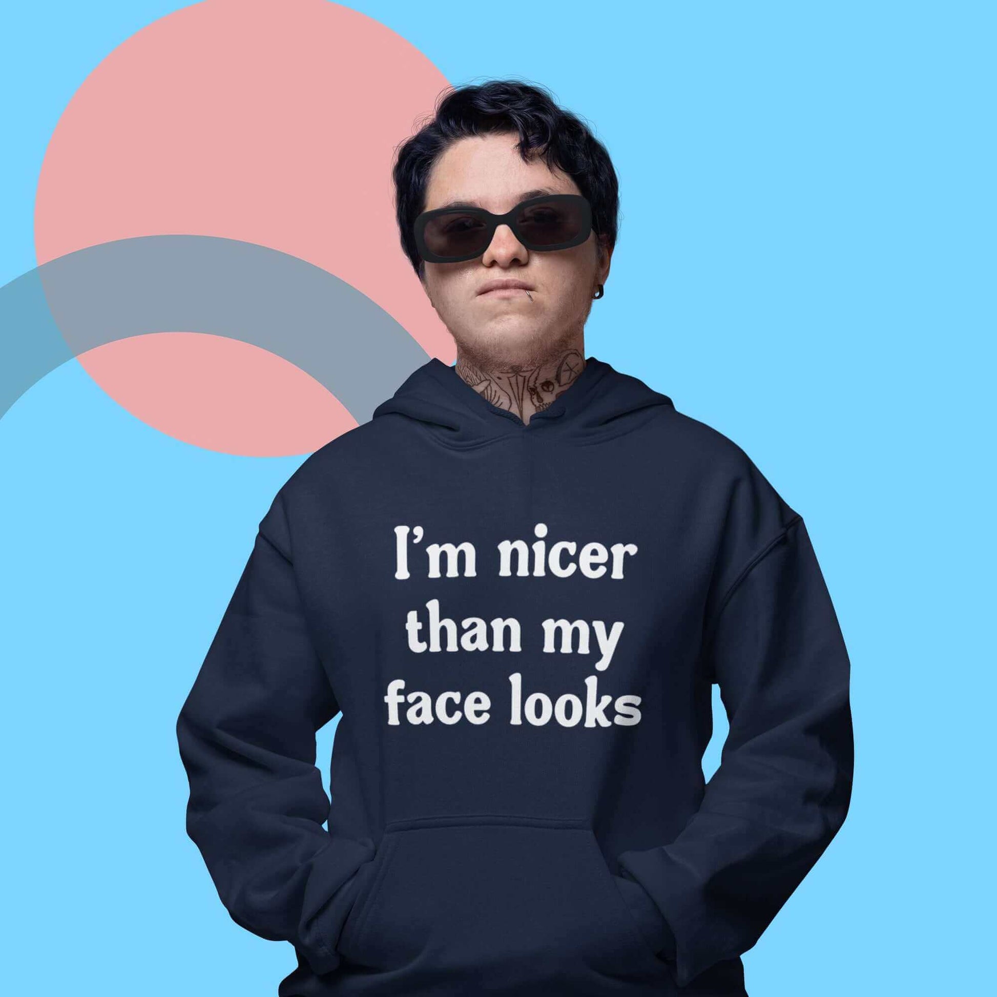 Tough looking woman wearing navy blue hoodie sweatshirt that says I'm nicer than my face looks printed on the front.